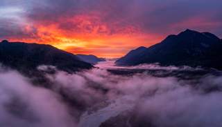 Stimmungsvoll liegt ein Tal unter Wolken im gleißend roten Sonnenaufgang.