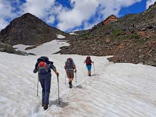 Drei Personen wandern über Schneefeld auf Berghütte zu