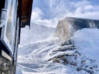 Zwei Berghütten im Schnee, der vom Wind verweht wird