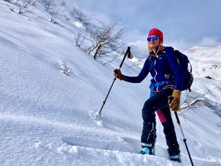 Skitourengeherin geht unberührte Schneelandschaft bei Sonnenschein hinauf