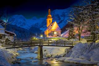 Verschneite Alpenlandschaft: Ein Bach, darüber eine Brücke und daneben eine Kirche.