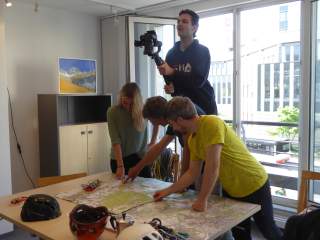 Nane, Helmut und Georg werden bei der Planung ihrer Anreisechallenge im Sektionsbüro gefilmt.
