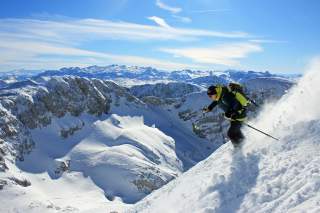 Skifahrer auf steiler Abfahrt mit Blick über schneebedeckte Alpen