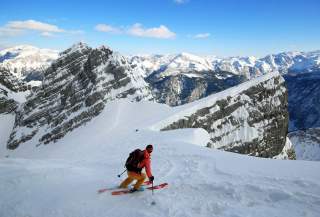 Mensch fährt mit Ski in verschneiter Berglandschaft und Ausblick auf Alpengipfel runter