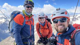 Drei Menschen machen Selfie auf hohem Gipfel.