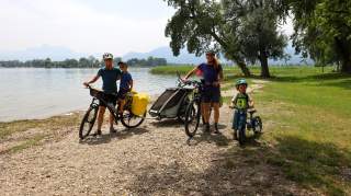 Zwei Frauen stehen mit zwei kleinen Jungen am Chiemsee. Sie haben ihre Fahrräder dabei.