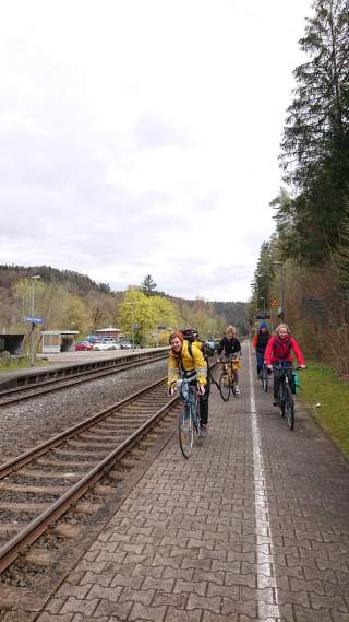 Vier Personen auf Fahrrädern, die auf einem Bahnsteig entlang auf die Kamera zufahren.