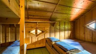 Ein holzvertäfelter Schlafrauf auf einer Hütte mit Doppelstockbett und Matratzenlager.