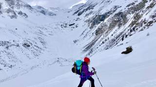 Skitourengeherin läuft Hang hoch über Tal entlang